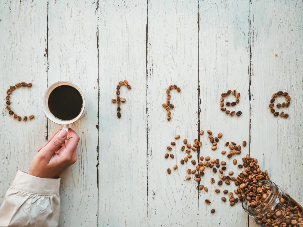 Coffee beans spell out 'coffee' on a wooden background. A woman's hand holds a cup of coffee.