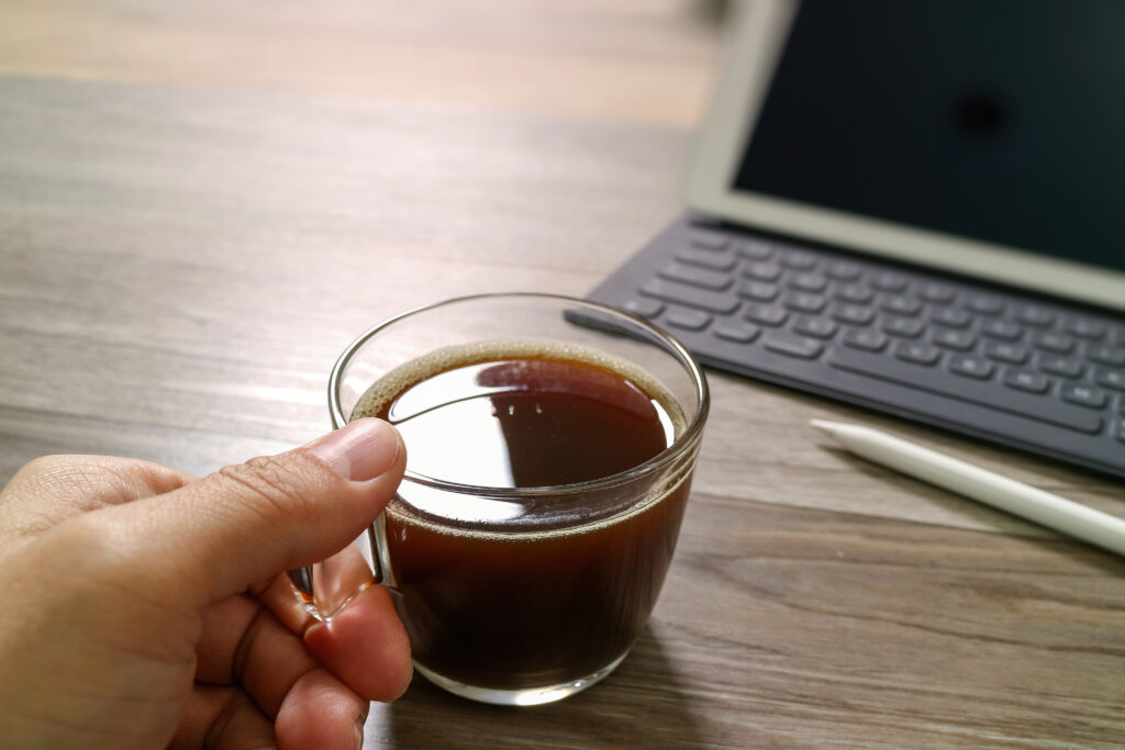 Hand holding a clear coffee mug by a laptop