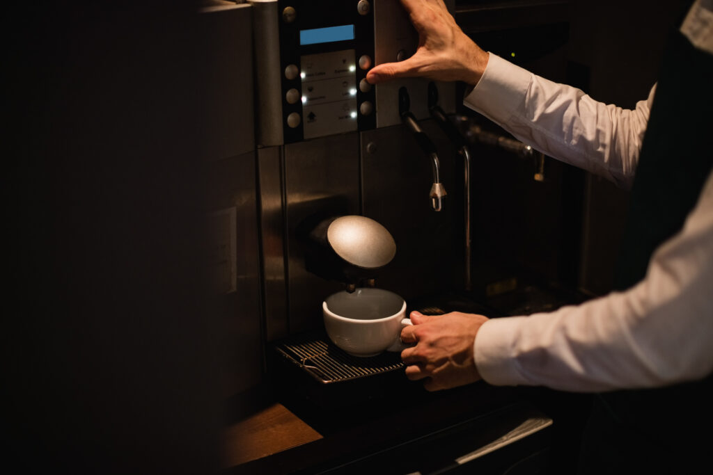 Employee using a coffee maker with a built-in grinder to prepare a cup of coffee.