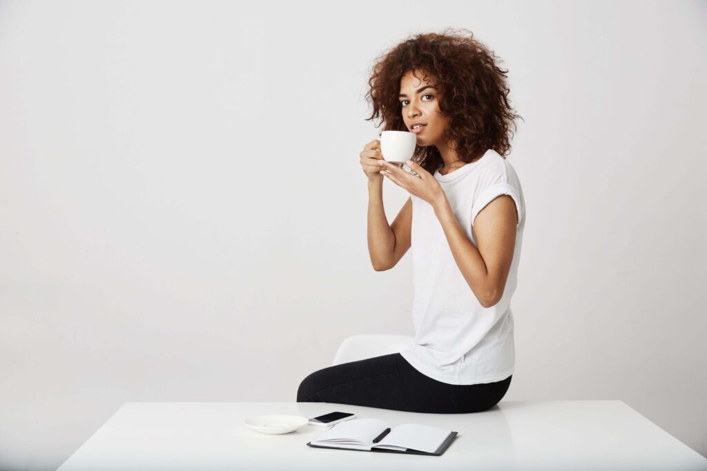 Lady posing on an office desk with stationery on it, sipping on a cup of coffee with one hand