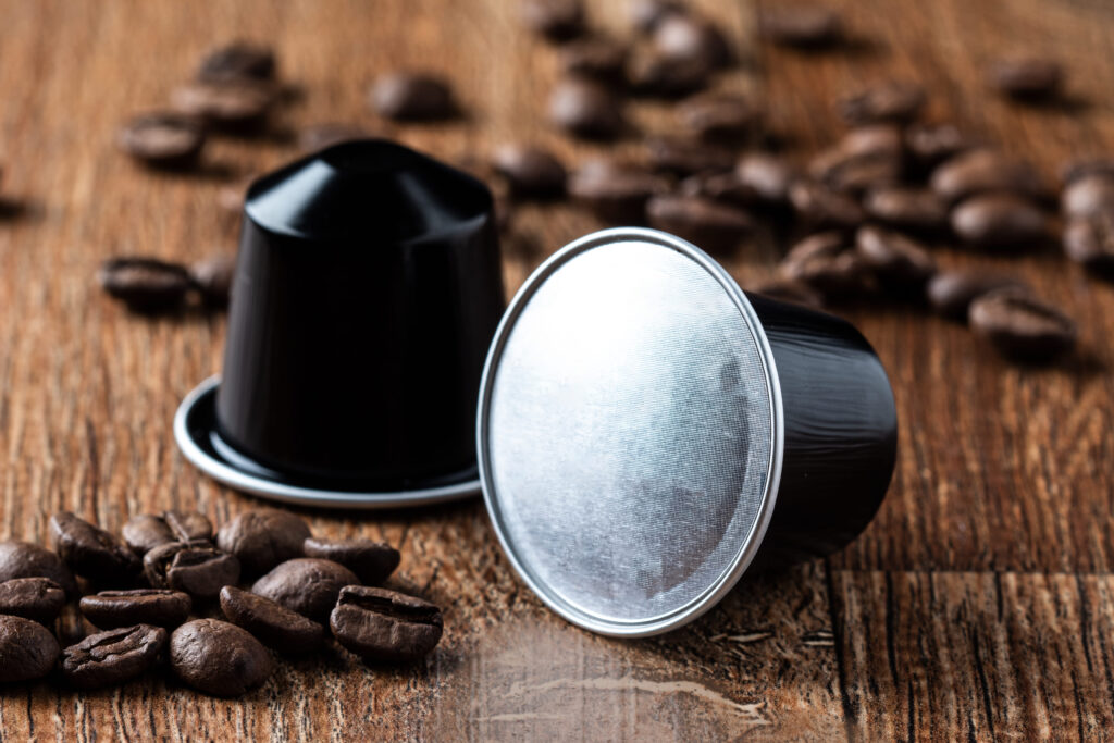 A close-up of two coffee pods and coffee beans sprinkled on a wooden table